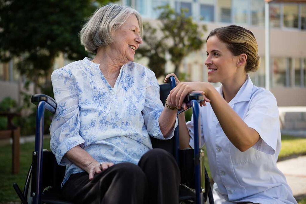 Seniors sitting together in a cozy living room, talking with a caregiver nearby.